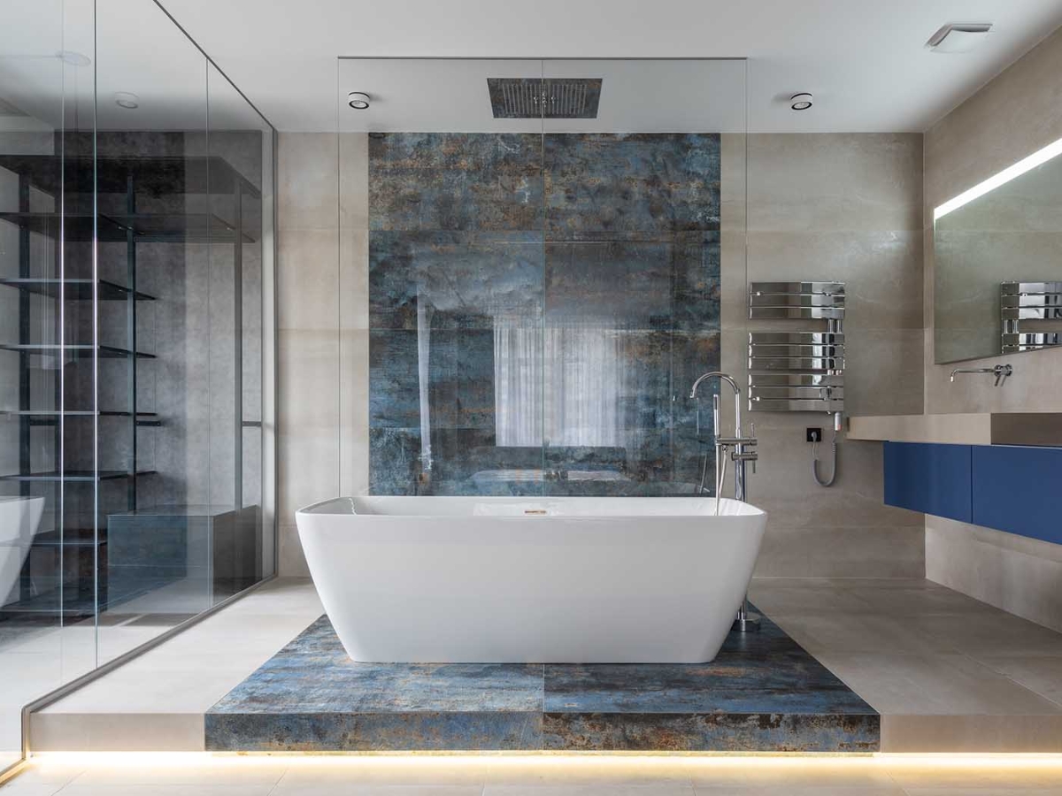 Bồn tắm nằm giữa không gian phòng tắm được thiết kế đơn giản với các góc cạnh trơn mịn và ánh sáng phản chiếu, tạo nên vẻ hiện đại và tinh tế.