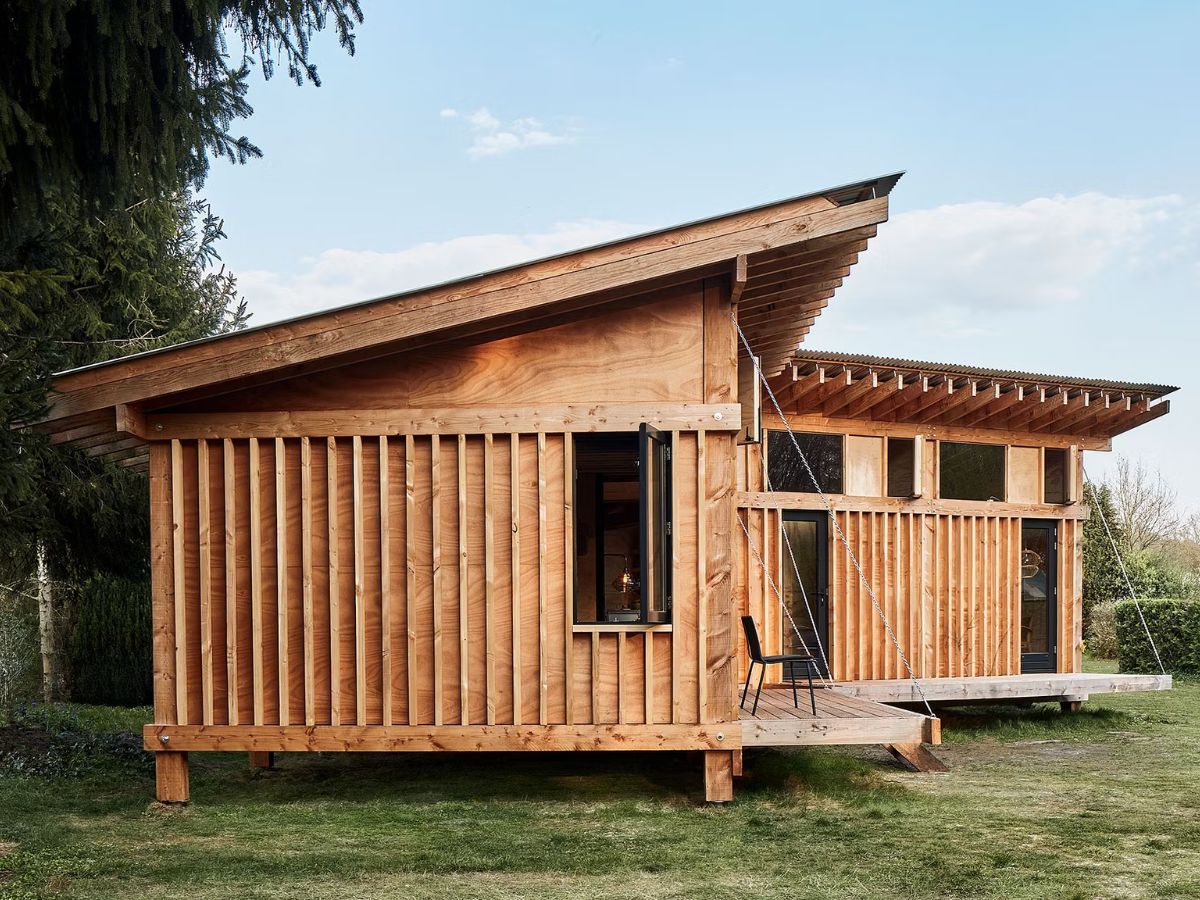Thiết kế nhà gỗ với kiểu dáng nhỏ gọn, mái nhà nghiêng và sân vườn xung quanh, tạo cảm giác ấm cúng và thân thiện
